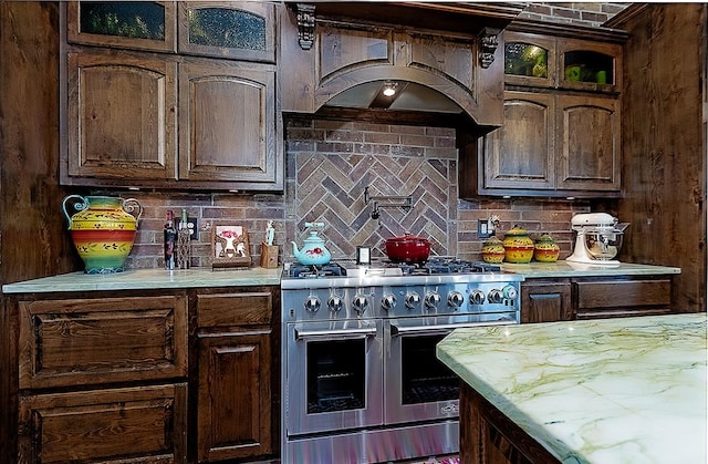 kitchen with backsplash, dark brown cabinets, double oven range, and premium range hood