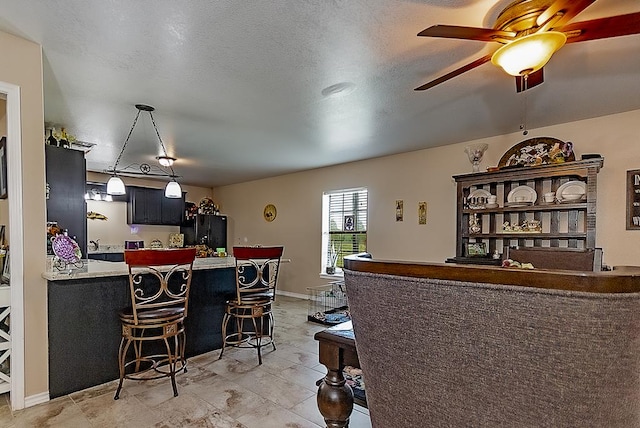 interior space featuring black refrigerator, a breakfast bar, a textured ceiling, ceiling fan, and pendant lighting