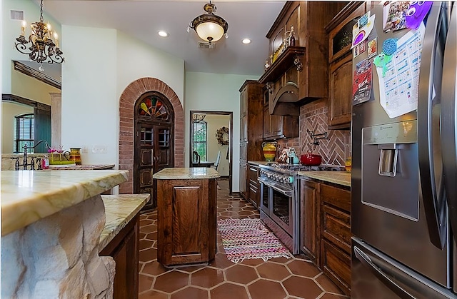 kitchen featuring appliances with stainless steel finishes, tasteful backsplash, dark brown cabinetry, a chandelier, and a center island