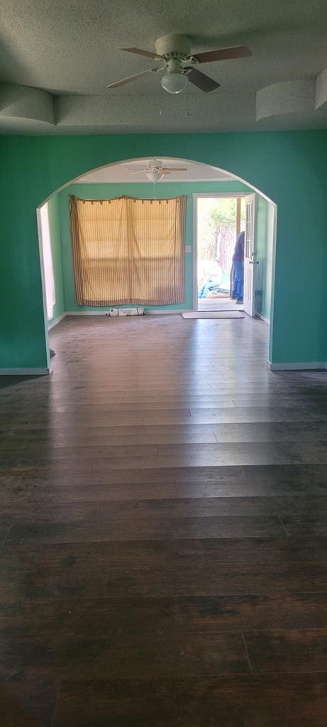 spare room with dark wood-type flooring, arched walkways, a textured ceiling, and baseboards