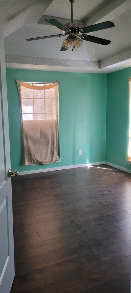 empty room featuring a textured ceiling, a ceiling fan, baseboards, vaulted ceiling, and dark wood finished floors