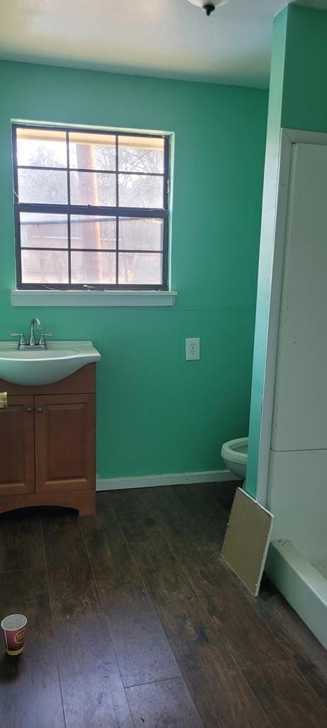 full bath with toilet, plenty of natural light, wood finished floors, and vanity