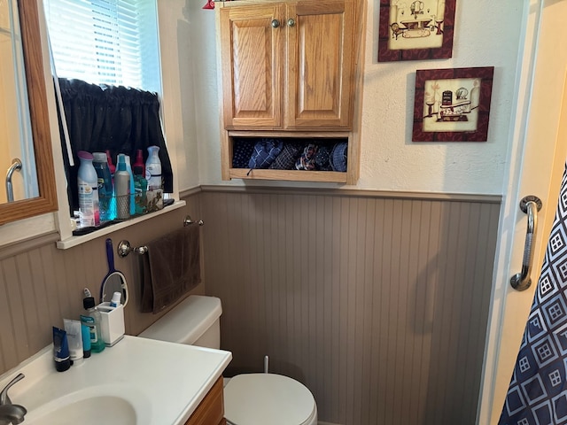 bathroom with toilet, a textured wall, wainscoting, and vanity