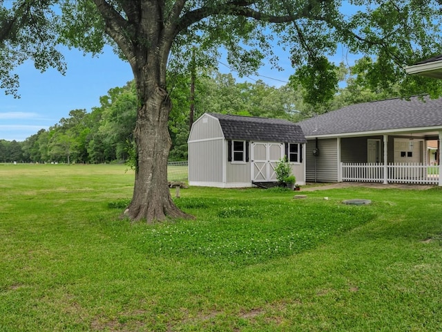exterior space featuring an outdoor structure, fence, a shingled roof, and a front lawn