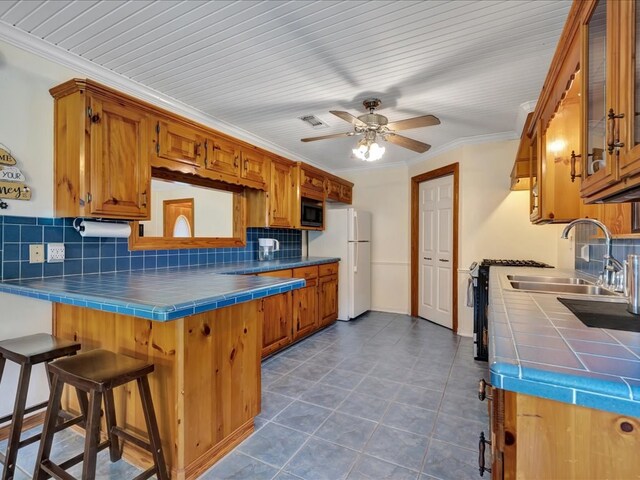 kitchen with backsplash, black microwave, freestanding refrigerator, and tile countertops