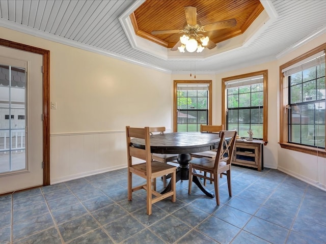 dining space featuring wainscoting, a ceiling fan, dark tile patterned floors, and a tray ceiling