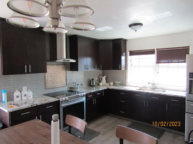 kitchen featuring electric range, sink, light stone counters, and wall chimney range hood