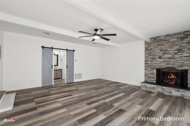 unfurnished living room featuring ceiling fan, visible vents, wood finished floors, beam ceiling, and a barn door