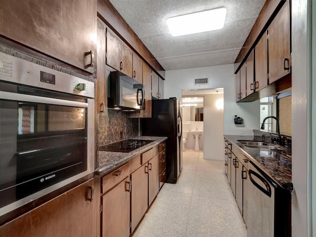 kitchen with black appliances, backsplash, dark stone countertops, and sink