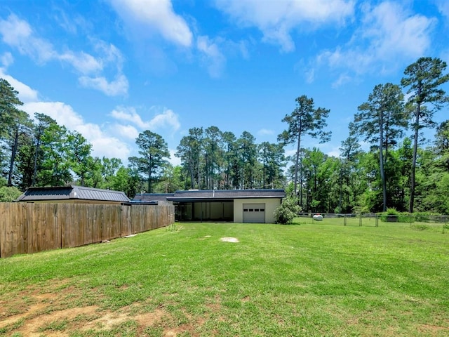 view of yard with driveway, a garage, and fence
