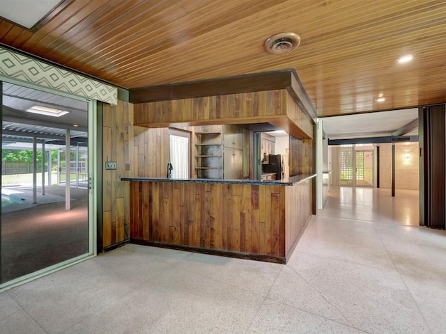 kitchen featuring kitchen peninsula, stainless steel fridge, wood walls, dark stone countertops, and wood ceiling