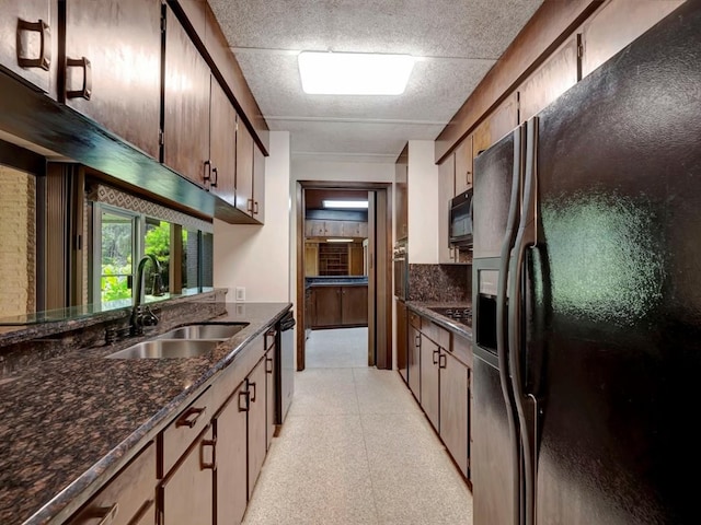 kitchen featuring black appliances, dark stone countertops, light floors, and a sink