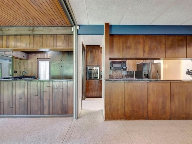 kitchen with stainless steel oven, refrigerator with ice dispenser, speckled floor, and black microwave