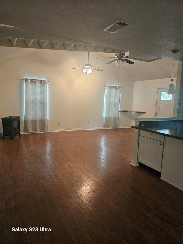 unfurnished living room with a ceiling fan, visible vents, a wood stove, dark wood finished floors, and lofted ceiling with beams