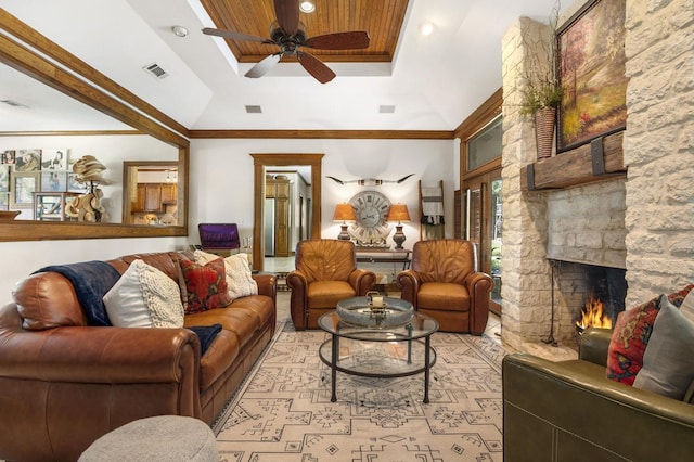 living room featuring a raised ceiling, a stone fireplace, ceiling fan, and crown molding