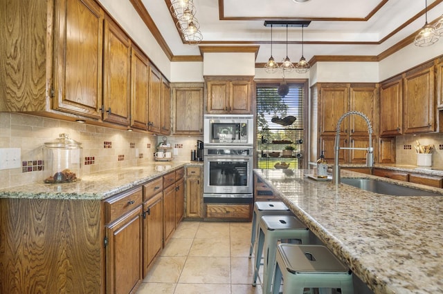 kitchen with backsplash, light stone counters, stainless steel appliances, sink, and hanging light fixtures