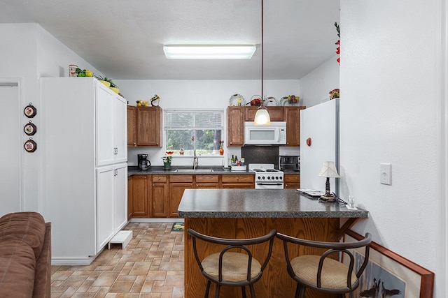 kitchen with sink, a kitchen breakfast bar, kitchen peninsula, pendant lighting, and white appliances