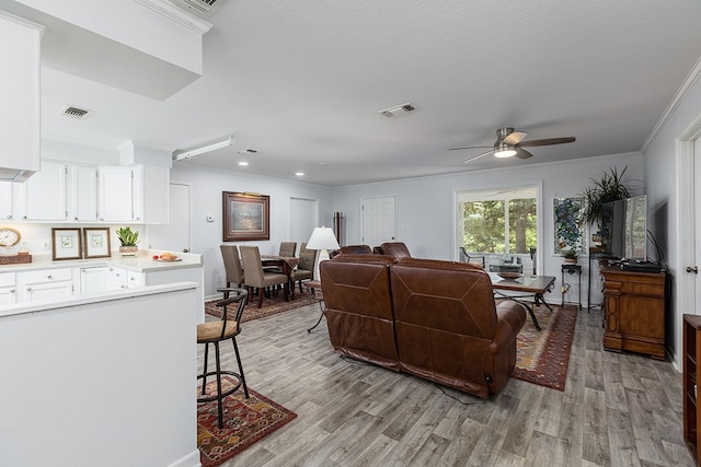 living room with ceiling fan, light hardwood / wood-style flooring, a textured ceiling, and ornamental molding