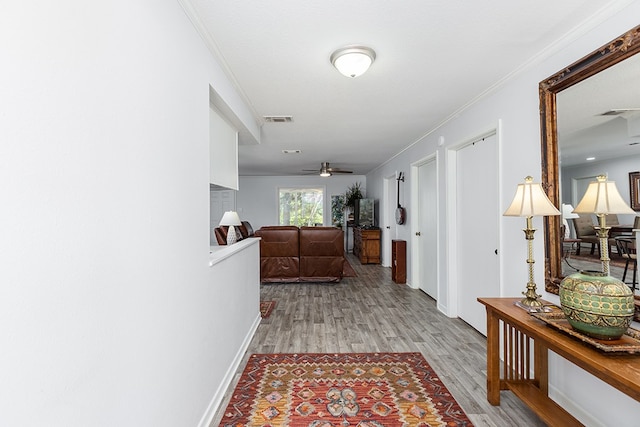 corridor with light hardwood / wood-style flooring, a textured ceiling, and ornamental molding