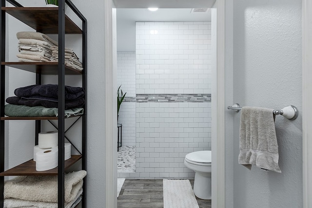 bathroom with hardwood / wood-style flooring, toilet, tile walls, and a tile shower