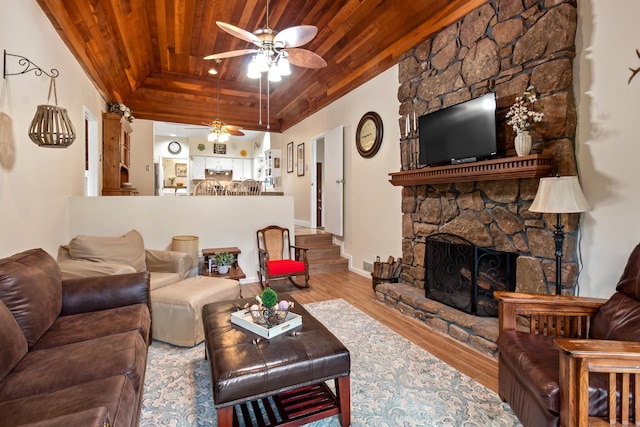 living area featuring ceiling fan, a stone fireplace, wooden ceiling, wood finished floors, and a raised ceiling