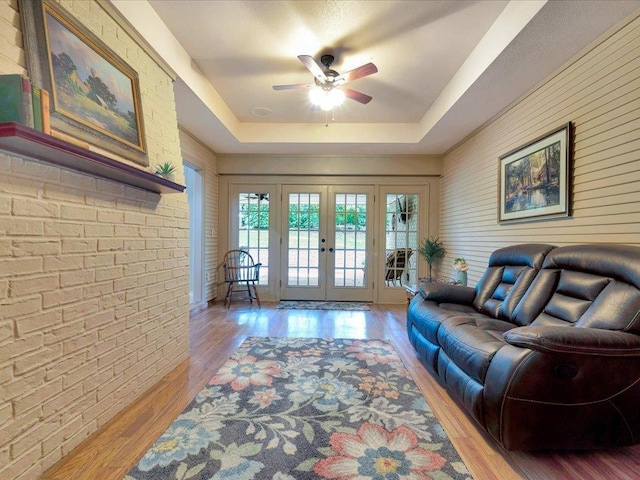 living room featuring ceiling fan, a raised ceiling, light hardwood / wood-style flooring, and french doors