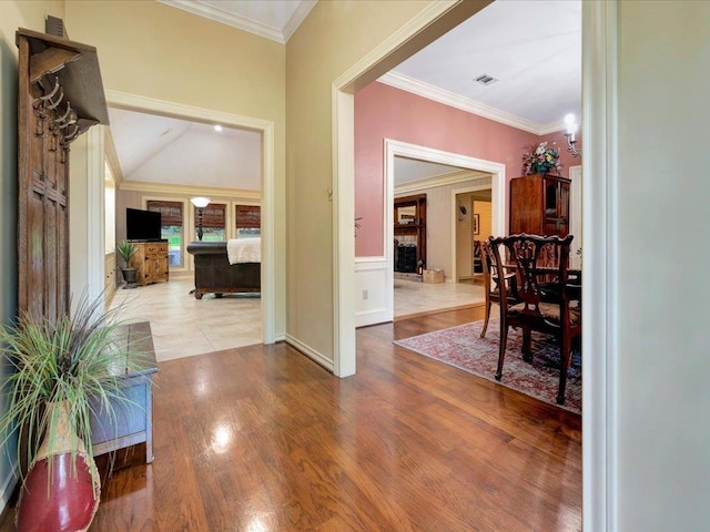 hallway with wood-type flooring, ornamental molding, and vaulted ceiling