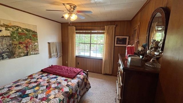 carpeted bedroom featuring crown molding, ceiling fan, and wooden walls