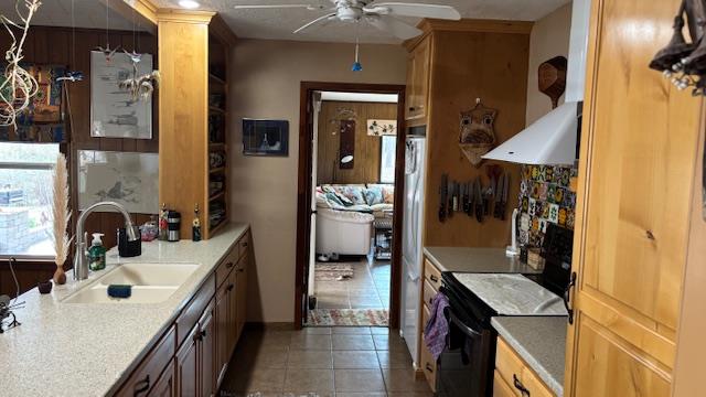 kitchen with wall chimney exhaust hood, black electric range oven, sink, dark tile patterned floors, and ceiling fan