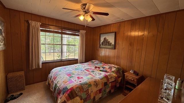 carpeted bedroom featuring ceiling fan and wood walls