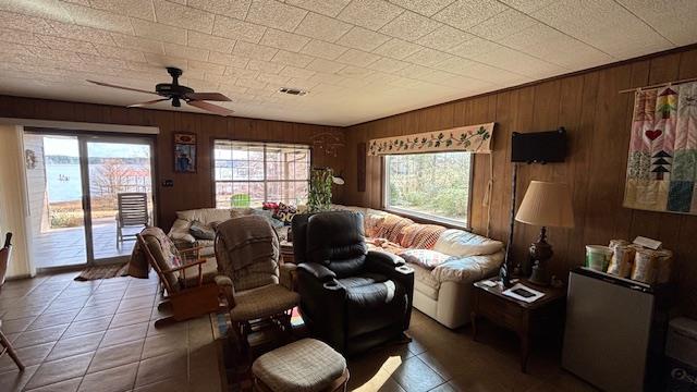 living room with ceiling fan, wooden walls, and dark tile patterned floors