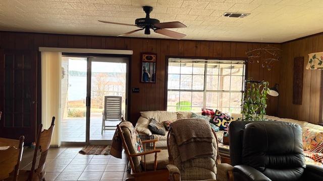 living room featuring light tile patterned flooring, ceiling fan, a textured ceiling, and wood walls