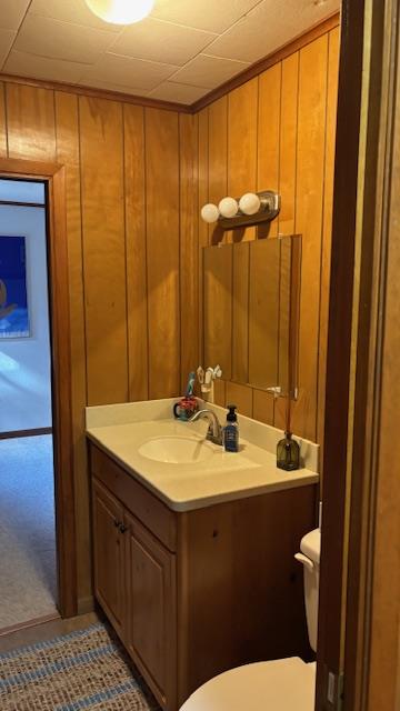 bathroom featuring vanity, wooden walls, and toilet