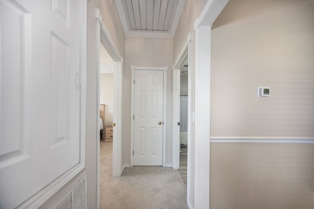 hallway featuring baseboards, visible vents, and light carpet
