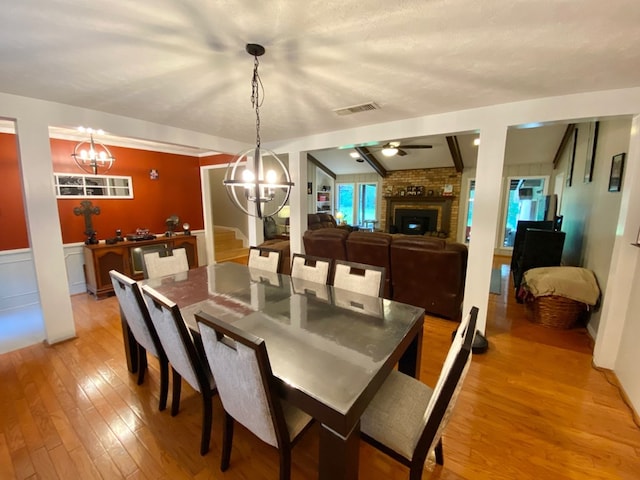 dining area featuring ceiling fan with notable chandelier, wood-type flooring, a textured ceiling, and a brick fireplace