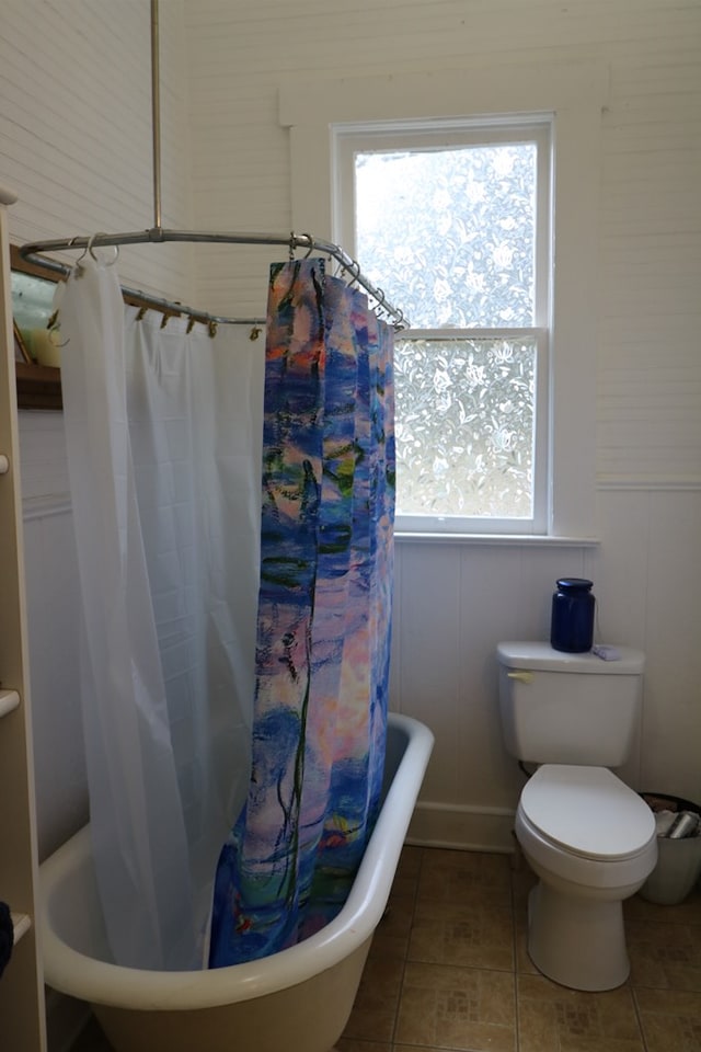 bathroom with toilet, tile patterned flooring, a wealth of natural light, and shower / bathtub combination with curtain