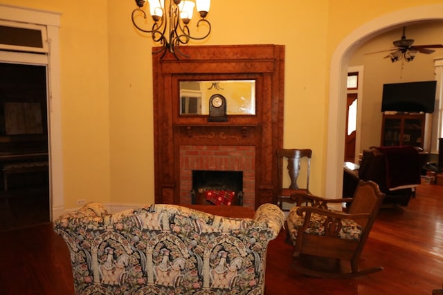 living room with a brick fireplace, ceiling fan with notable chandelier, and wood-type flooring