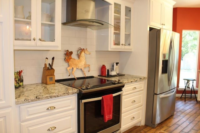 kitchen featuring appliances with stainless steel finishes, light wood-type flooring, tasteful backsplash, wall chimney exhaust hood, and white cabinetry