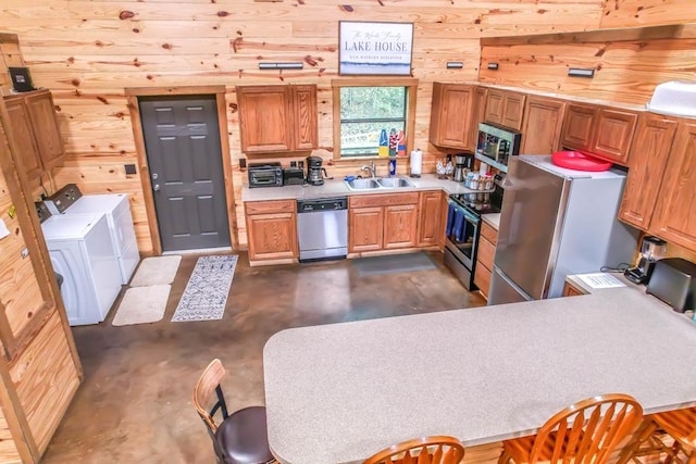 kitchen with appliances with stainless steel finishes, sink, washer and clothes dryer, and wood walls