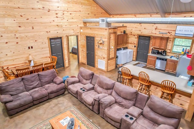 living room with vaulted ceiling with beams, wooden walls, sink, and independent washer and dryer