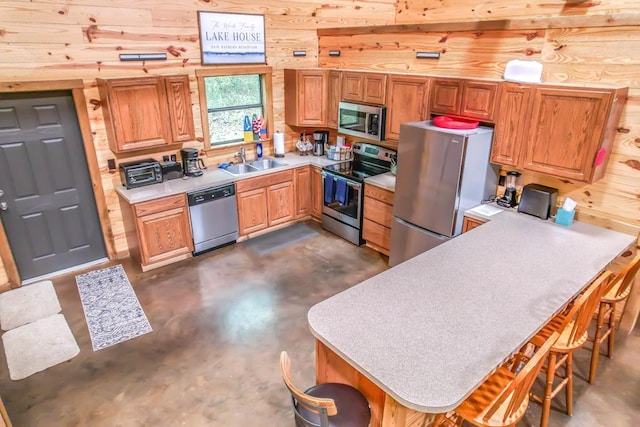 kitchen with sink, wooden walls, appliances with stainless steel finishes, kitchen peninsula, and a breakfast bar area