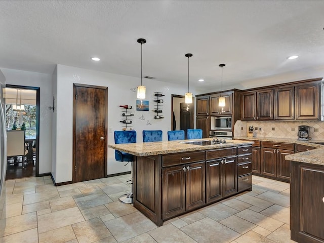 kitchen featuring light stone counters, a kitchen island, a kitchen breakfast bar, decorative light fixtures, and backsplash