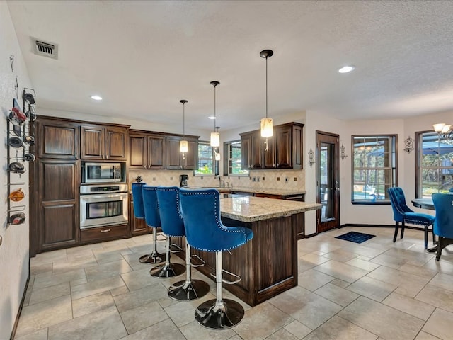 kitchen with light stone countertops, appliances with stainless steel finishes, a kitchen island, and a wealth of natural light