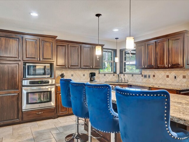 kitchen with sink, hanging light fixtures, stainless steel appliances, a breakfast bar, and a kitchen island