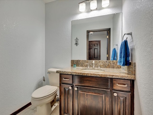 half bathroom with tile patterned flooring, toilet, vanity, and a textured wall