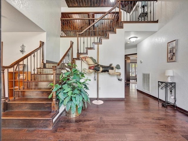 stairway with visible vents, baseboards, wood finished floors, and a towering ceiling