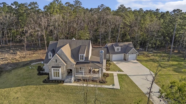 view of front of house featuring driveway, stone siding, a wooded view, a front yard, and metal roof