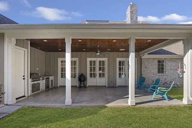 exterior space featuring a patio, an outdoor kitchen, french doors, board and batten siding, and ceiling fan