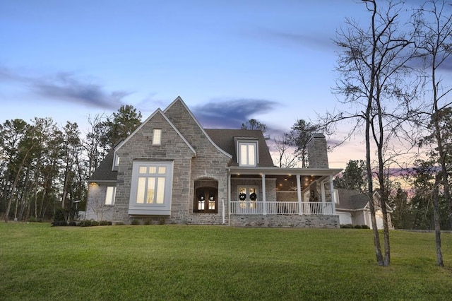 view of front of home featuring stone siding, a porch, a chimney, and a yard