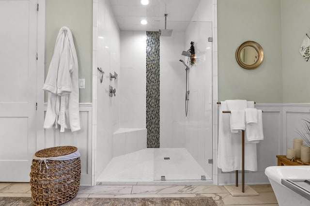 full bath featuring a wainscoted wall, a stall shower, a freestanding tub, a decorative wall, and marble finish floor